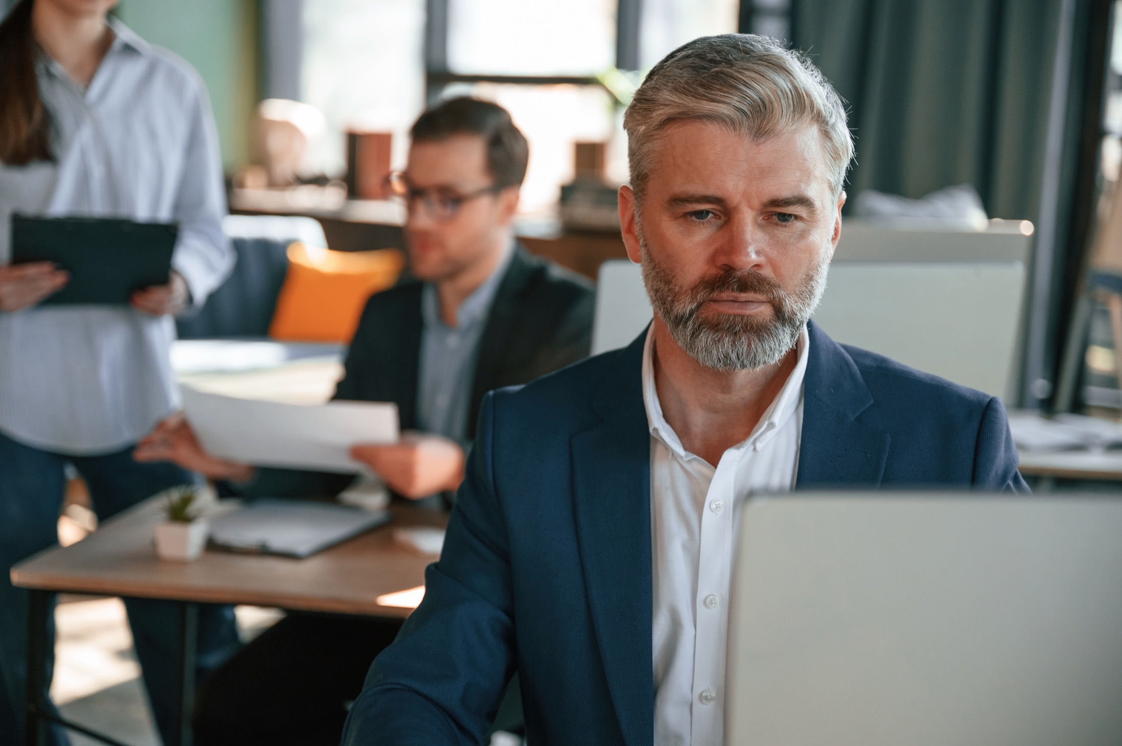 Business leader working at a laptop with colleagues in the background